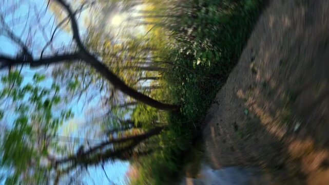 A low altitude FPV view flying over a stream, under trees in Valley Stream State Park on a sunny day. The FPV drone camera dolly in, roll left and pan right 180 degrees to dolly out in the area.