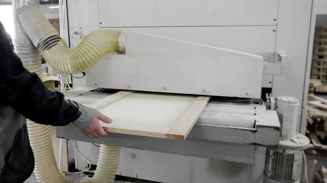 Worker removing finished wooden panel from industrial woodworking machine in furniture production factory.