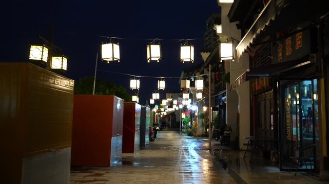 Traditional Chinese ancient street at night with hanging lanterns and wet stone pavement after rain