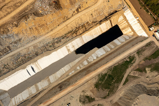 Brasov, Romania - 28 April 2026: Aerial view of a large industrial landfill site featuring a deep rectangular pit lined with white material and surrounding dirt roads.