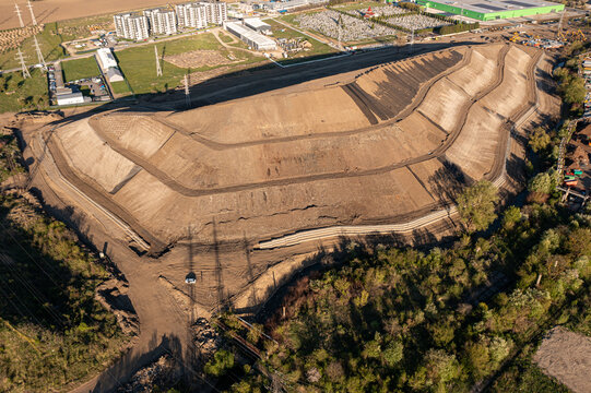 Brasov, Romania - 28 April 2026: Aerial view of a large terraced earthwork construction site with dirt paths and surrounding industrial buildings under bright sunlight.