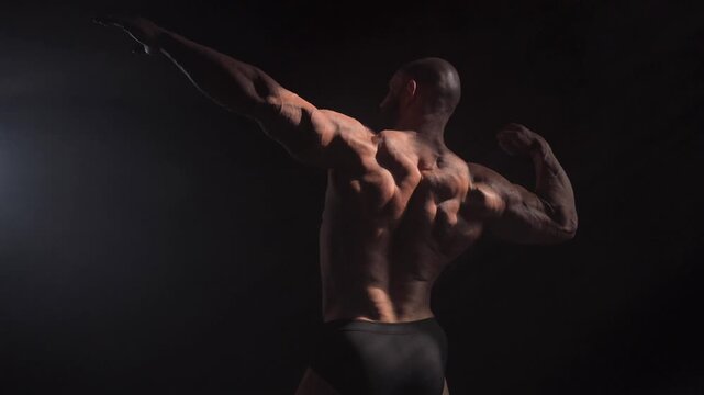 A male bodybuilder poses in shorts, showing off his back muscles.