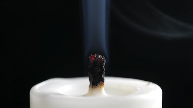 A close-up shot of a burning candle wick with smoke rising against a dark background, creating a serene and peaceful atmosphere