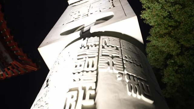 A stone scripture tower illuminated by artificial lighting at night with carved Buddhist inscriptions