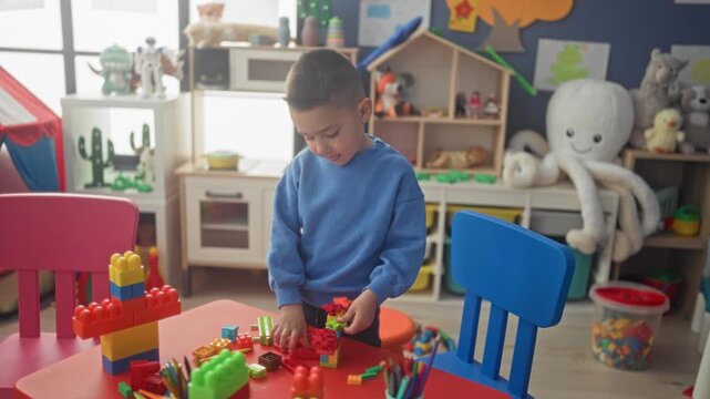 Boy building colorful toy blocks with bare hands at a preschool classroom table, stacking and assembling plastic bricks; concentration creativity.