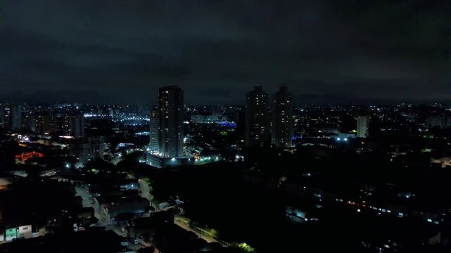 Vista urbana noturna em formato vertical com pr&eacute;dios residenciais iluminados e skyline moderno, ideal para uso mobile e redes sociais.