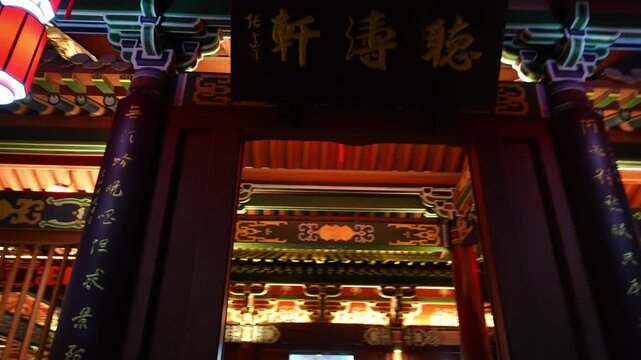 Traditional Chinese paifang gate at night with red lanterns and inscribed plaque