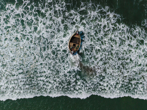 Cox's Bazar, Bangladesh - 10 March 2026: Aerial view of a traditional wooden fishing boat navigating through white foamy waves in the turquoise sea.