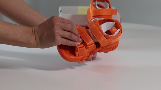 Woman examines sandals, unfastens and fastens hook-and-loop. Check children's sandals, choose shoes for the child. Check out the bright orange velcro sandals with an open heel