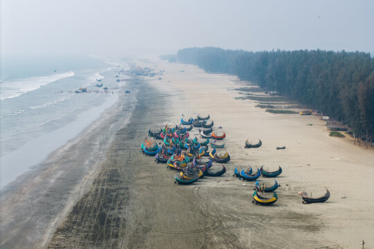 Cox's Bazar, Bangladesh - 10 March 2026: Aerial view of colorful moon-shaped fishing boats parked on the sandy shore of the world's longest natural sea beach under a hazy sky.