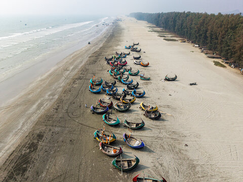 Cox's Bazar, Bangladesh - 10 March 2026: Aerial view of traditional colorful moon boats parked on the sandy shore of the world's longest natural sea beach under a hazy sky.