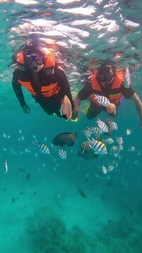 Happy couple in snorkeling mask dive underwater with tropical fishes in coral reef sea in Weh Island Sabang, Indonesia. Show by hands divers sign of love and heart. 