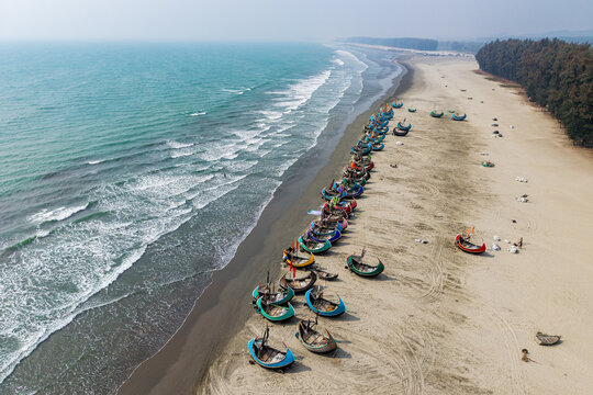 Cox's Bazar, Bangladesh - 10 March 2026: Aerial view of traditional colorful moon boats lined up on the sandy shore of the world's longest natural sea beach with turquoise waves and pine trees.