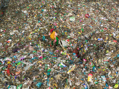 Aminbazar, Bangladesh - 26 January 2025: Aerial view of a woman scavenger walking through a vast expanse of colorful plastic waste and garbage at a landfill.