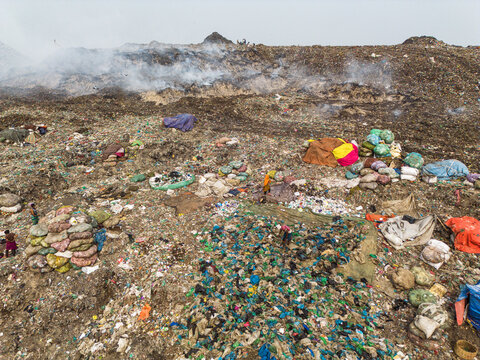 Aminbazar, Bangladesh - 26 January 2025: Aerial view of the Aminbazar landfill with workers scavenging among vast piles of waste and smoke rising from burning trash under a hazy sky.