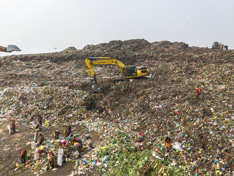 Aminbazar, Bangladesh - 26 January 2025: Aerial view of the Aminbazar landfill with yellow excavators moving waste and many people scavenging through piles of garbage under a hazy sky.