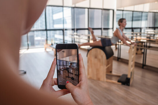 Woman recording Pilates Ladder Barrel workout on smartphone in modern fitness studio
