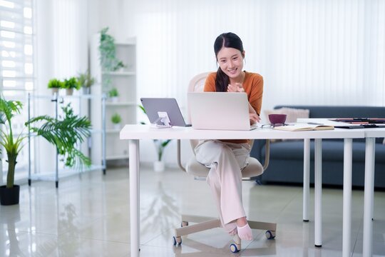 Asian businesswoman hybrid work setup modern office desk using laptop computer smiling happy professional employee working remote flexible workspace bright