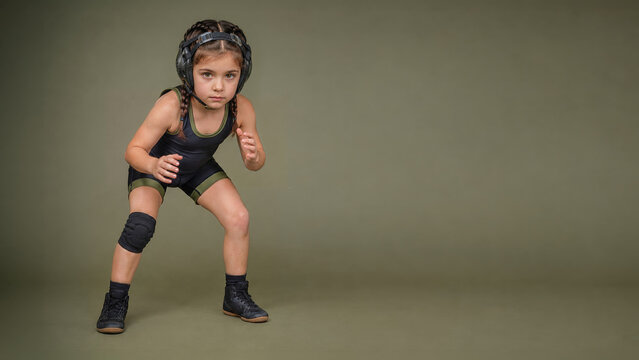 Young girl in wrestling headgear and singlet holds a ready stance on an olive studio background with wide copy space.