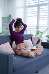 Obraz premium Asian women freelancer remote worker adjust hair using laptop computer sitting cross leg on sofa work from home modern apartment living room with natural