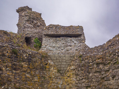 Camouflaged Second World War gun emplacement built into the ancient defensive stone walls of a ruined castle under an overcast sky (Pevensey, England, United Kingdom)