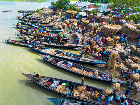 Islampur, Bangladesh - 05 September 2025: Aerial view of traditional wooden boats docked along a busy riverbank where workers are loading large bundles of jute under a bright sun.