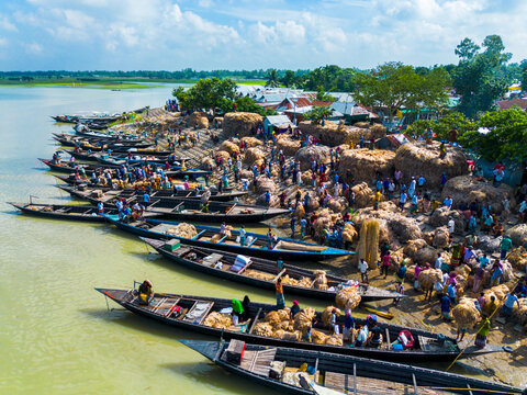 Islampur, Bangladesh - 05 September 2025: Aerial view of a bustling riverbank market with workers loading large bundles of jute onto traditional wooden boats under a bright sky.