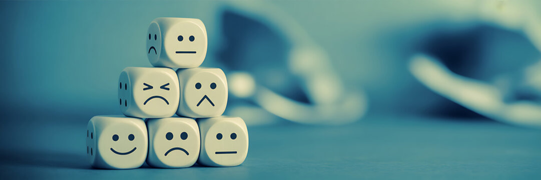 A stack of white dice with different emoticon faces on each side on a blue surface with blurred background