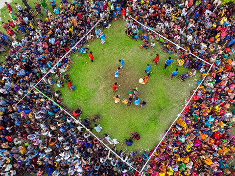 Nilphamari, Bangladesh - 01 May 2026: Aerial view of a large crowd of people gathered around a square grassy arena for a traditional event with musicians and participants.
