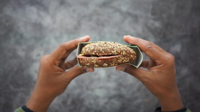 Hand holding a sandwich with brown bread and filling