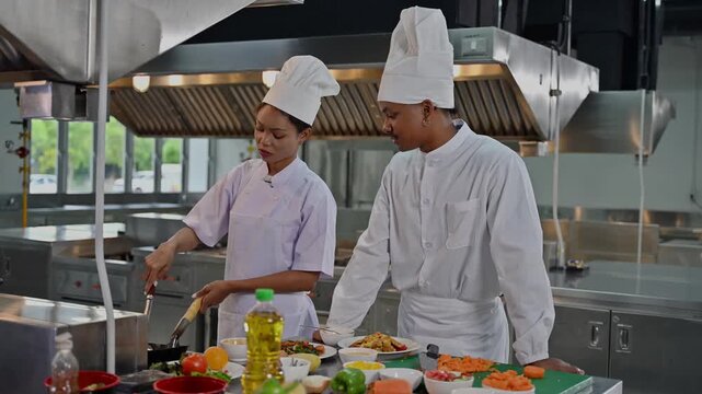 Male senior culinary student teaching his junior female classmate how to cook in a commercial training kitchen