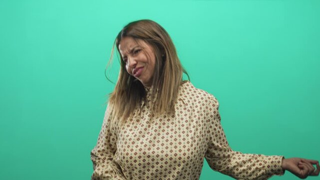 Woman strumming an air guitar with hand gesture and animated facial expression against a green studio backdrop, patterned blouse visible; playful joy.