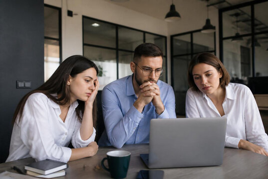 Dedicated business team collaborating intensely on a laptop, analyzing data and problem-solving with focused expressions in a modern office setting
