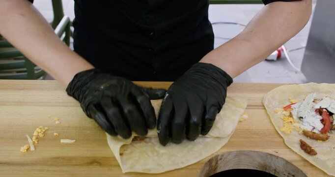 Pita sandwich. Preparing burrito. Chef cooking shawarma on kitchen table. Gloved hands wrapping flatbread with meat vegetables sauce.