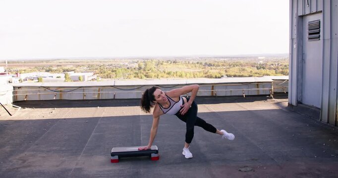 Rooftop workout. Sportive trainer. Motivated flexible female athlete performing squat physical exercise developing active skill outdoor.