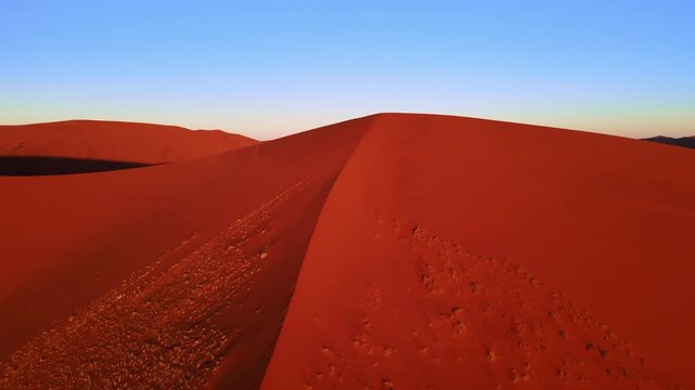 Drone footage captures the vast Namib Desert with towering red sand dunes glowing under the low setting sun, revealing breathtaking panoramic views of shifting patterns and timeless desert beauty.