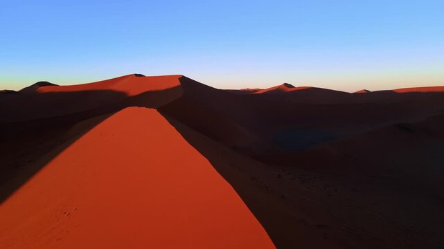 Drone footage captures the vast Namib Desert with towering red sand dunes glowing under the low setting sun, revealing breathtaking panoramic views of shifting patterns and timeless desert beauty.