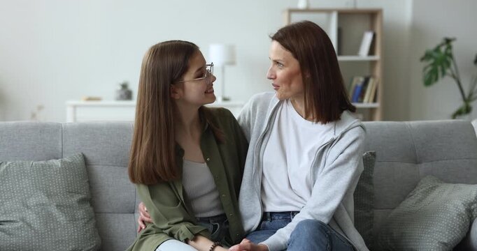 Mother and daughter talking sit on couch in living room at home, showing love, understanding and warm relationships between teen and parent. Family connection, interpersonal communication, bonding