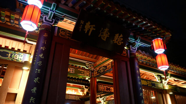 Traditional Chinese paifang gate at night with red lanterns and inscribed plaque