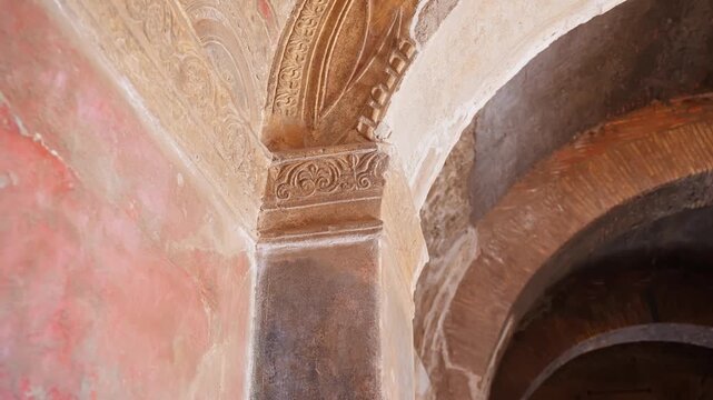 Ornate Pompeii interior detail featuring a decorated pilaster capital, stucco arch, and painted wall surface inside a preserved Roman room.