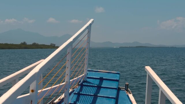 Front view from boat deck with blue crates sailing calm tropical waters with mountains and islands in distance. &middot; 4K DCI 25fps