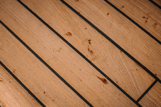 High-angle close-up of a weathered teak wood boat deck with black caulking lines and natural grain texture