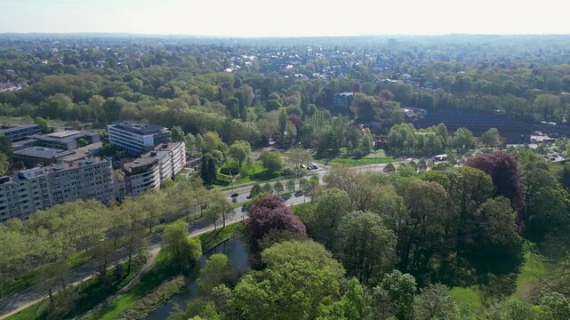 Aerial view of lush green parkland, a calm canal, and residential apartment buildings under a clear sky in Woluwe-Saint-Pierre, Bruxelles, Belgium.