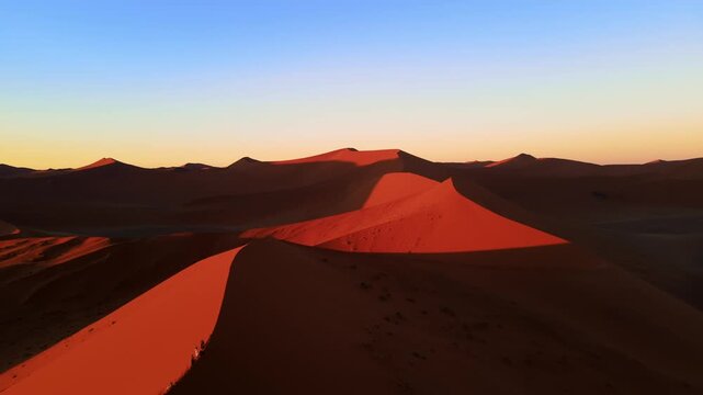 Drone footage captures the vast Namib Desert with towering red sand dunes glowing under the low setting sun, revealing breathtaking panoramic views of shifting patterns and timeless desert beauty.