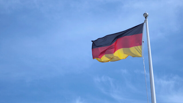 German National Flag Waving on a White Pole Against Blue Sky
