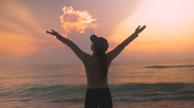 Back view of female traveler enjoying peaceful sunrise over the sea with open arms. Cinematic beach lifestyle footage with warm light, freedom, self care and uplifting travel wellness atmosphere.