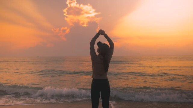 Back view of female traveler enjoying peaceful sunrise over the sea with open arms. Cinematic beach lifestyle footage with warm light, freedom, self care and uplifting travel wellness atmosphere.