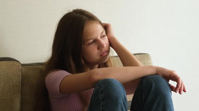 Sad teen girl sitting on couch and covering face by hands. Concept of sadness, depression, mental health problems, loneliness, anxiety, abuse and stress