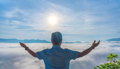 A man stands peacefully above a sea of clouds at sunrise in Bao Loc, Vietnam. Stretching his arms toward the morning sun. © huythoai
