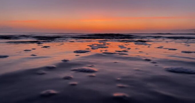 Serene sunset over a tranquil beach with gentle waves and foam, creating a peaceful atmosphere
